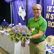 Wayne Geeslin holding his Best in Show violet in front of the awards table